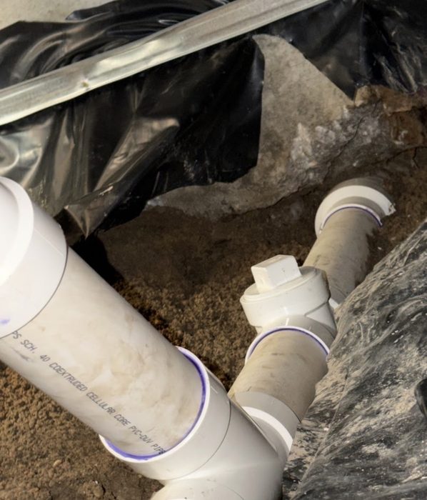 Exposed underground pipe installation in a concrete floor trench during plumbing repair work.